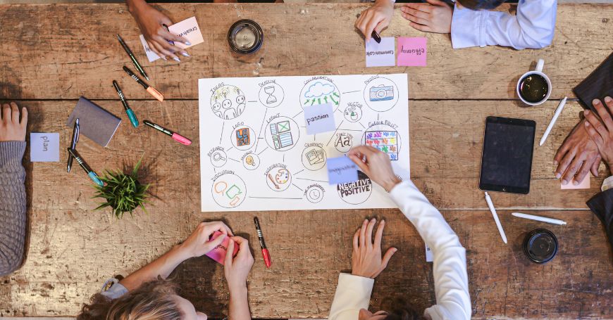 Team di lavoro in brainstorming attorno a un tavolo, con laptop e termini di marketing che suggeriscono lo sviluppo di un payoff.